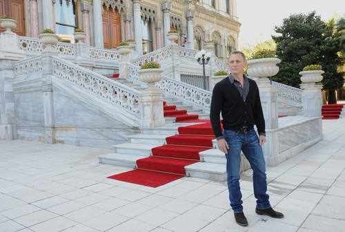 Un look casual para Daniel Craig con vaquero, camisa oscura lisa y chaqueta negra con botas oscuras.